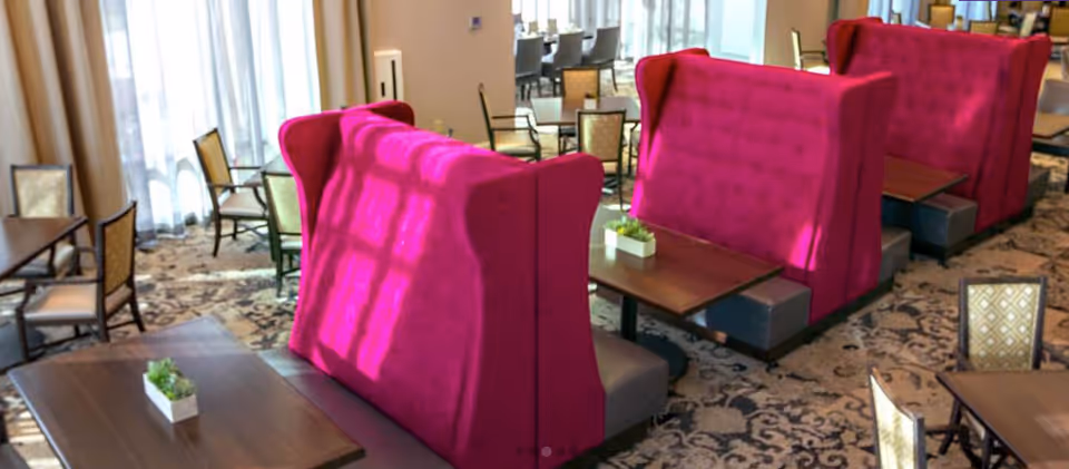 Dining area with high-backed magenta upholstered booths, wooden tables, and patterned carpet.
