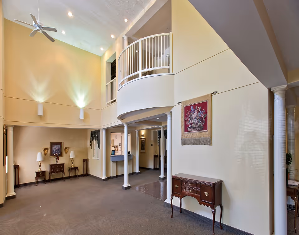 Spacious two-story entry lobby with a curved balcony, columns, decorative furniture and wall hangings.
