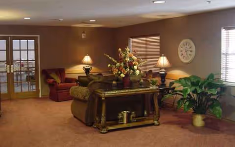Cozy senior living room with sofas, plants, lamps, and a floral centerpiece.