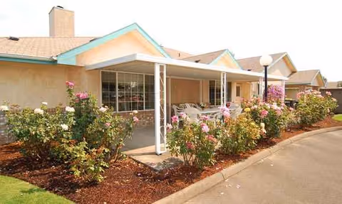 Front view of a senior living facility with a covered entrance and rose landscaping.