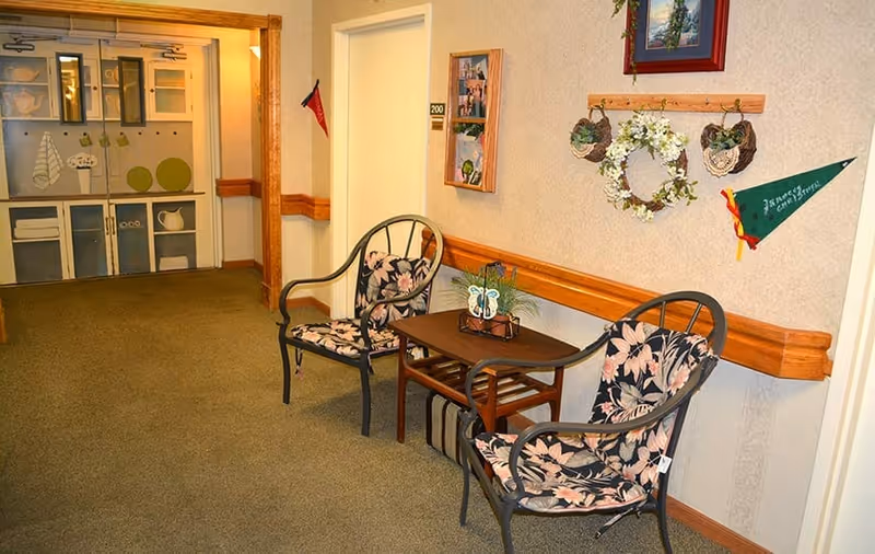 Hallway seating area with two floral-cushioned chairs, a small table, and wall decorations.