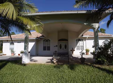 Front view of a single-story senior living facility with palm trees and a covered entrance