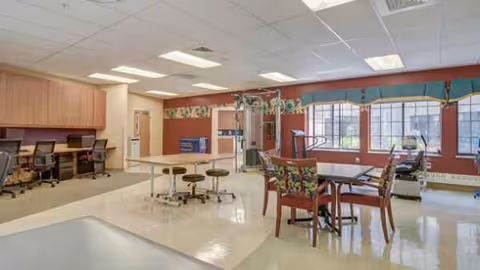 Interior common area with tables, chairs, and exercise equipment in a senior living facility.