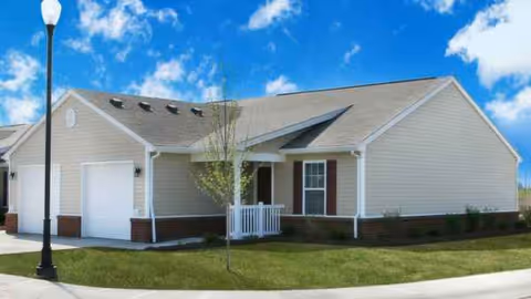 Single-story beige senior living villa with white trim, front entrance, and manicured lawn.