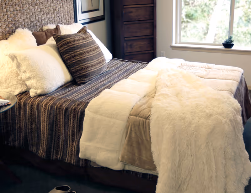 A neatly made bed with layered blankets and decorative pillows beside a window in a cozy bedroom.
