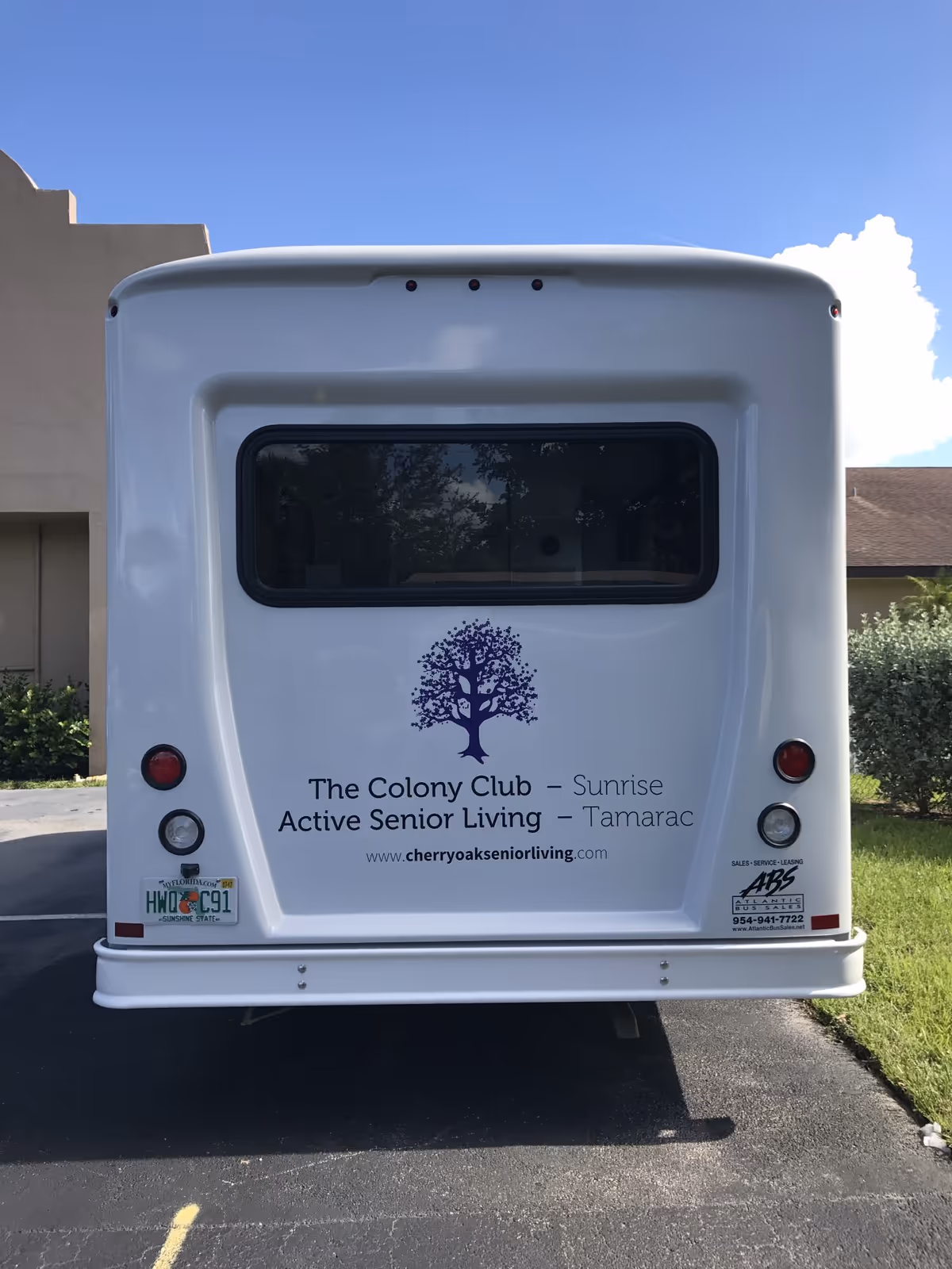 Rear view of a white shuttle bus displaying The Colony Club Active Senior Living logo and website.
