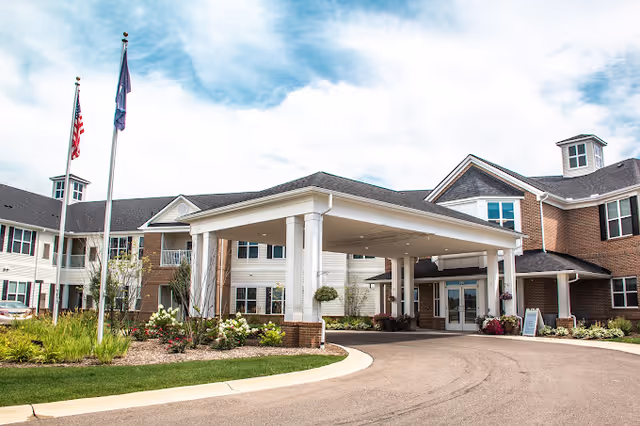 Front entrance of Olivia's Assisted Living showing a covered porte-cochere, flagpoles, and landscaped driveway.