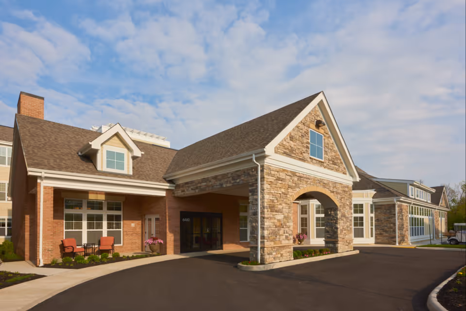 Exterior view of Dublin Retirement Village showing a building with a stone and brick facade, a covered entrance, large windows, and a driveway under a partly cloudy sky.