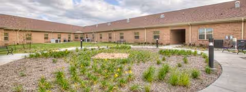 Exterior view of a brick senior living courtyard with circular garden bed and benches.