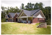 Row of single-story brick and siding cottages with porches on a grassy lawn bordered by trees.