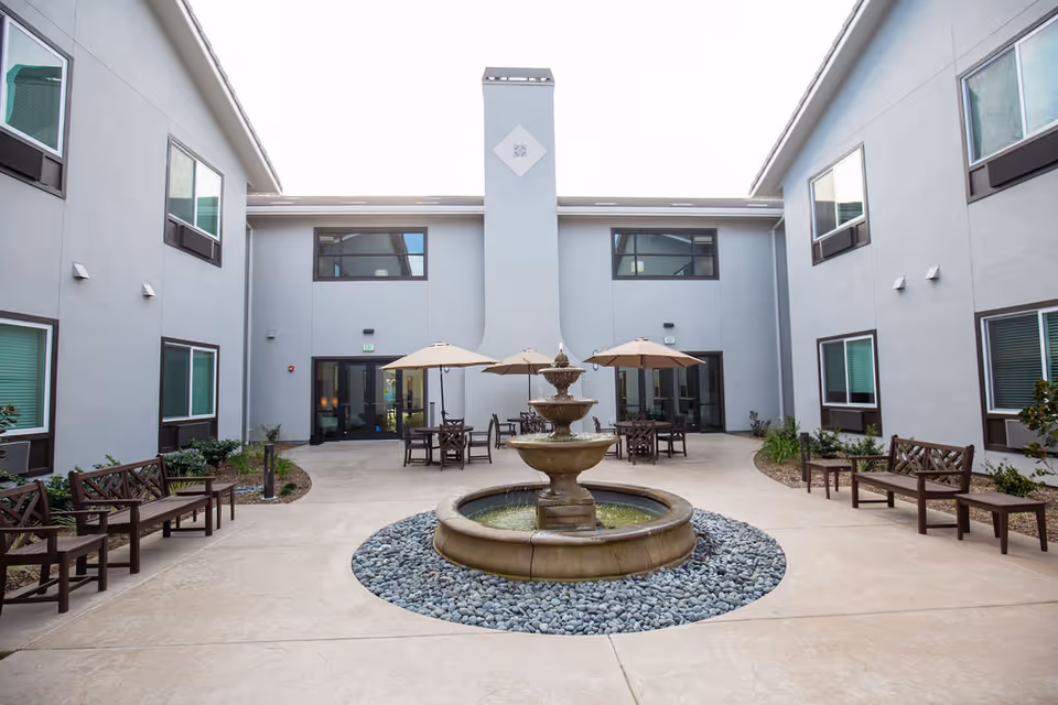 Courtyard at Belmar Senior Living featuring a central fountain, seating, and umbrellas.