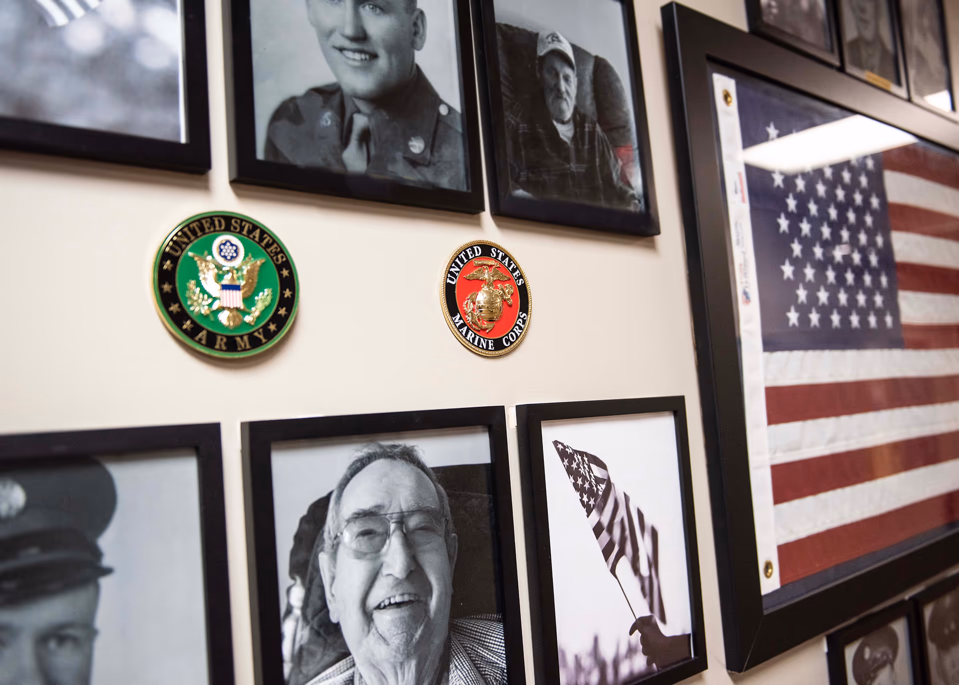 Framed black-and-white portraits, military insignia, and an American flag displayed on an interior wall.