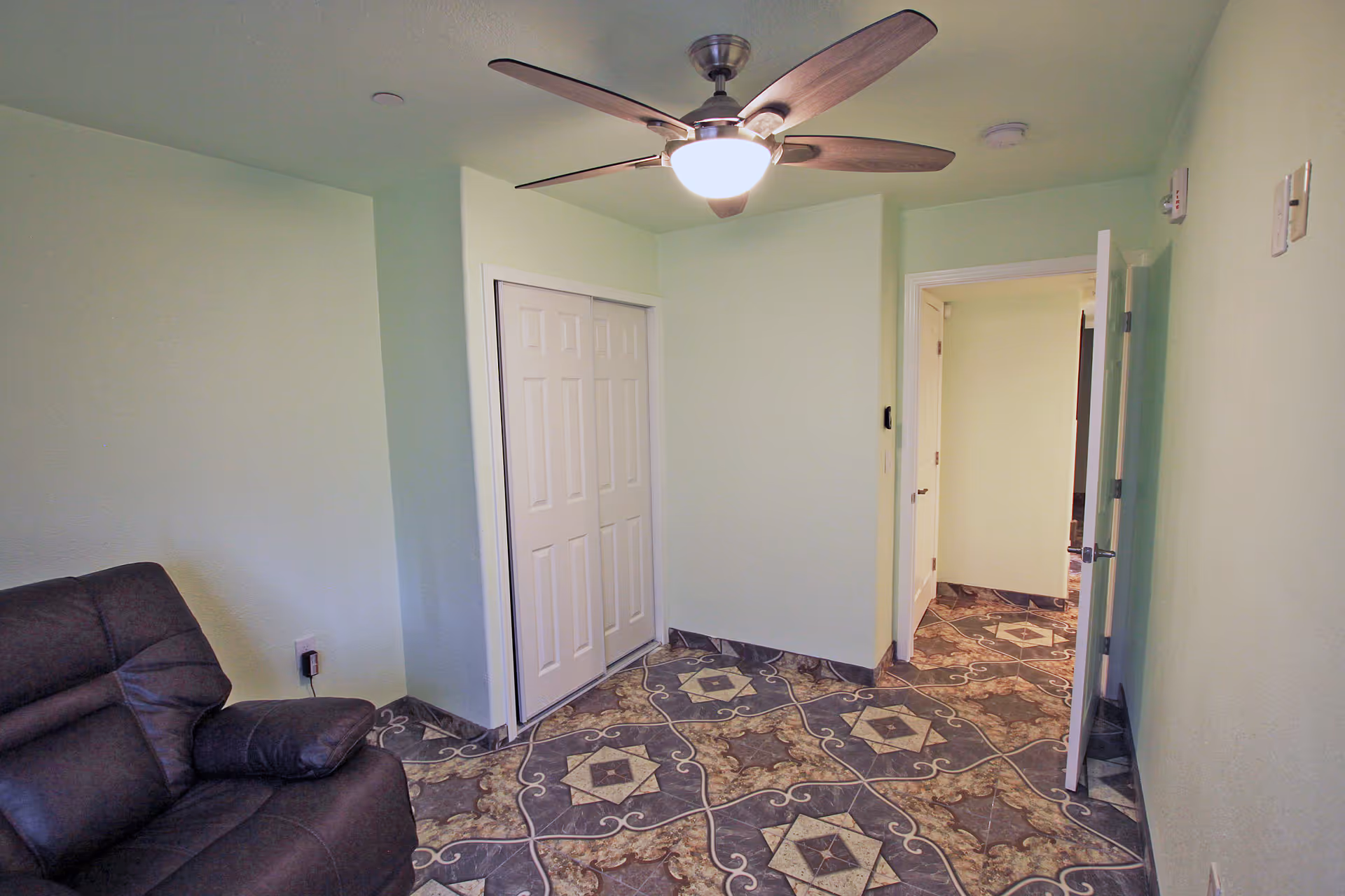 Mint-green walls, a ceiling fan, patterned tile floor, and a hallway with a couch.