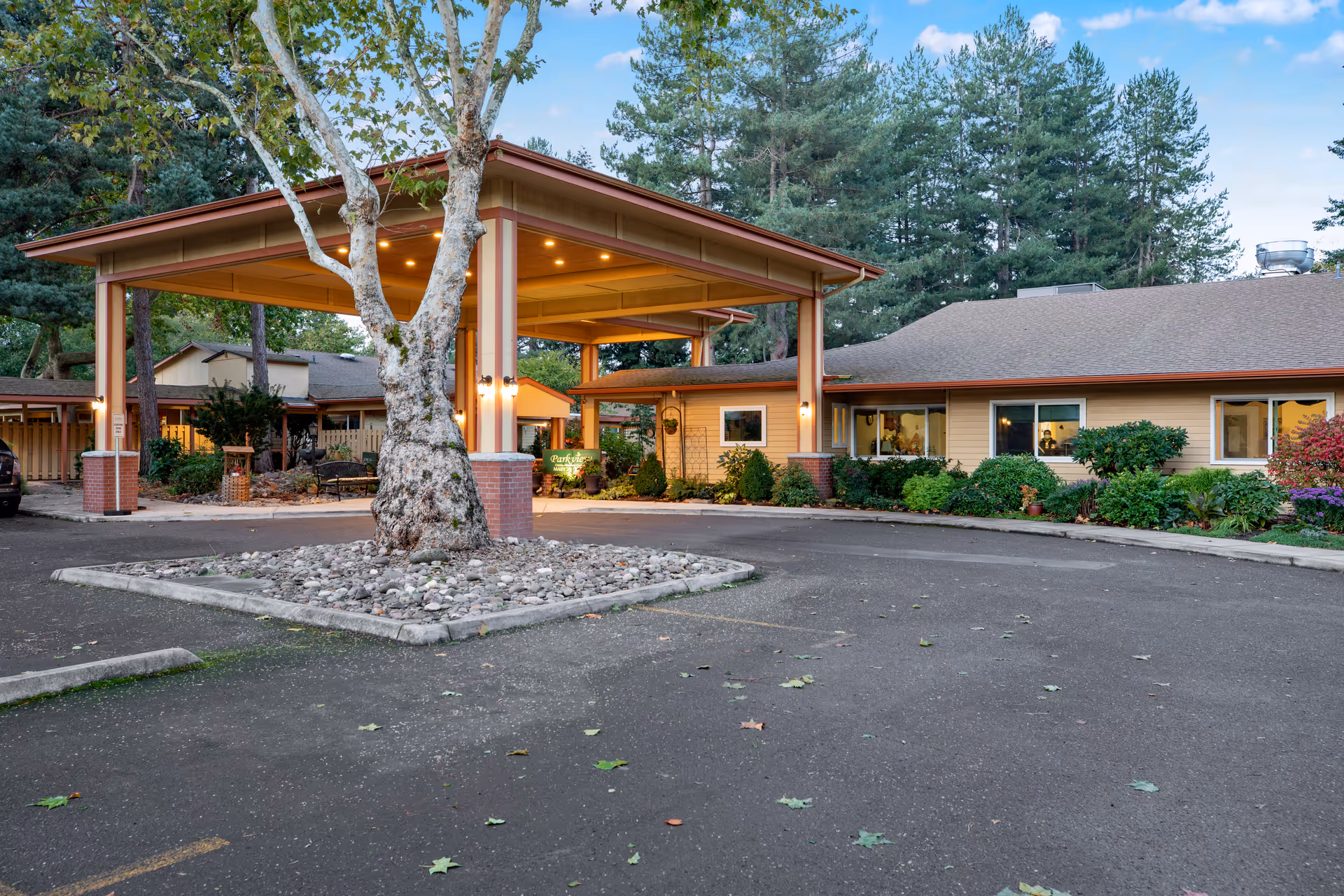 Entrance area of Parkview Christian Retirement Community featuring a covered drop-off with brick pillars, surrounded by trees and greenery, with a paved driveway and parking spaces.