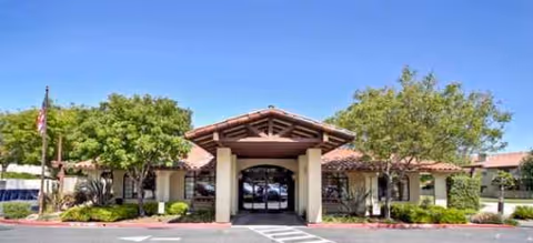 A single-story senior living facility entrance with a covered porte-cochère and landscaping.