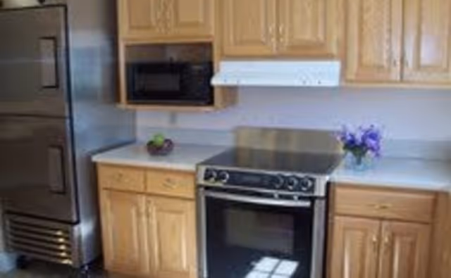 Kitchen with stainless steel refrigerator, electric range, microwave and wooden cabinets.