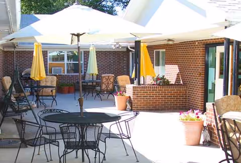 Outdoor patio at Laramie Care Center with tables, chairs, umbrellas, and potted plants.