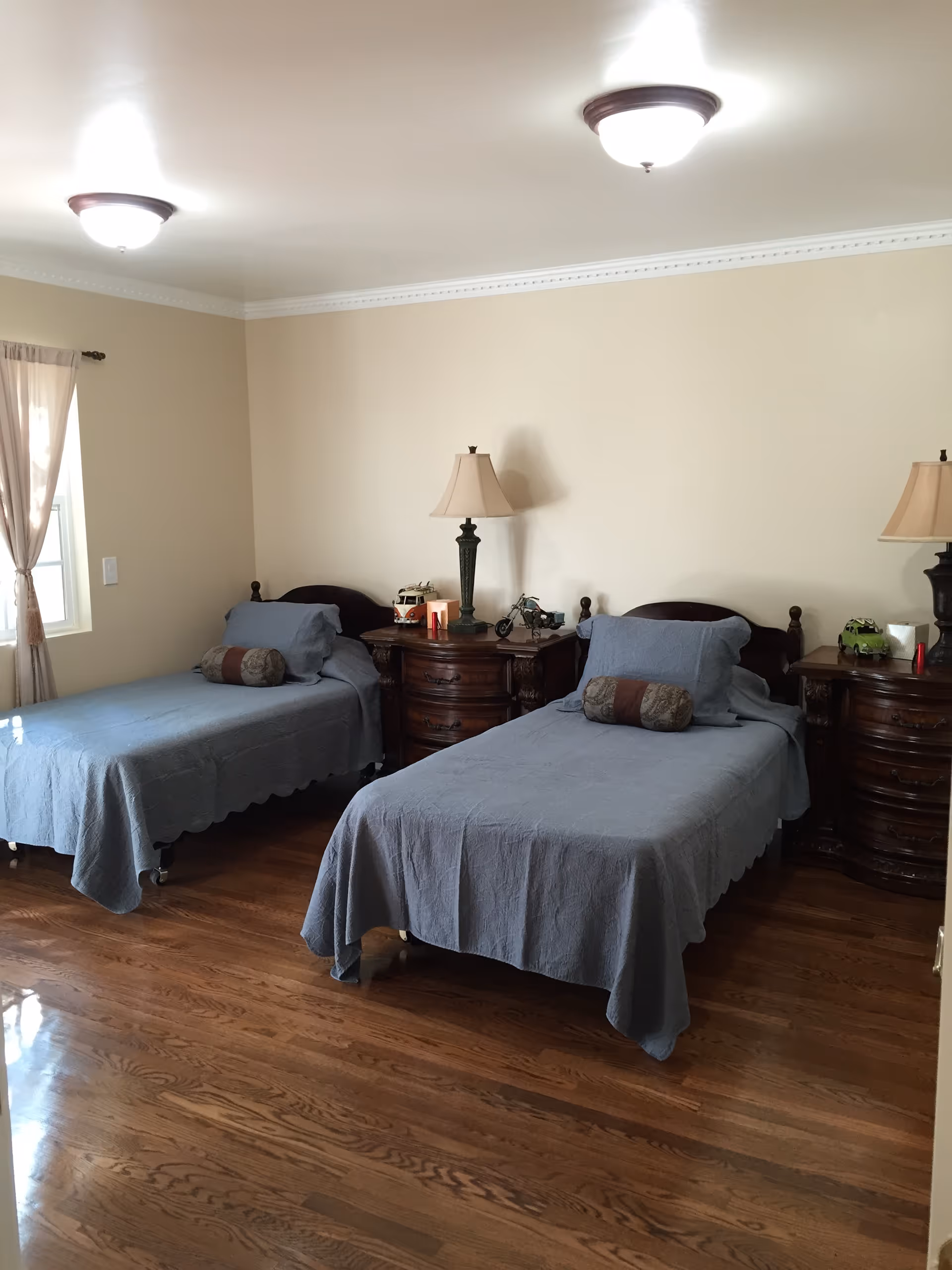 Bright bedroom with two twin beds covered in blue bedspreads and wooden nightstands with lamps.