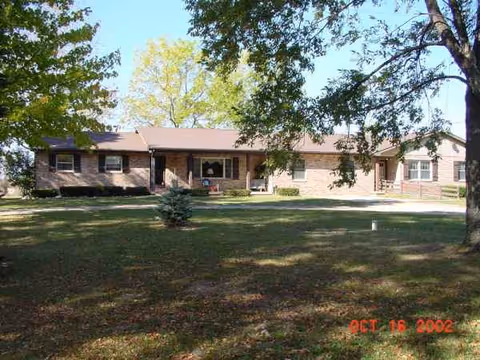 Serenity House senior living facility front entrance with brick exterior, lawn, and trees.