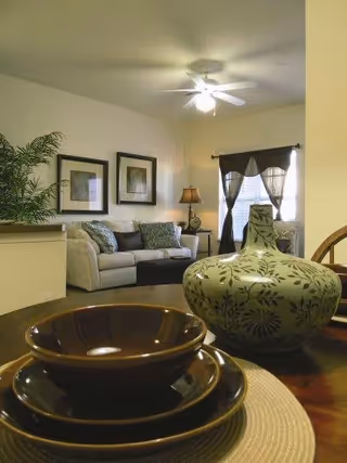 Furnished living room with a sofa, framed artwork, ceiling fan, and decorative bowls and a patterned vase in the foreground.
