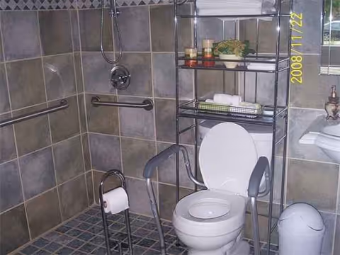 Accessible bathroom with toilet, walker, grab bars, and storage shelf.