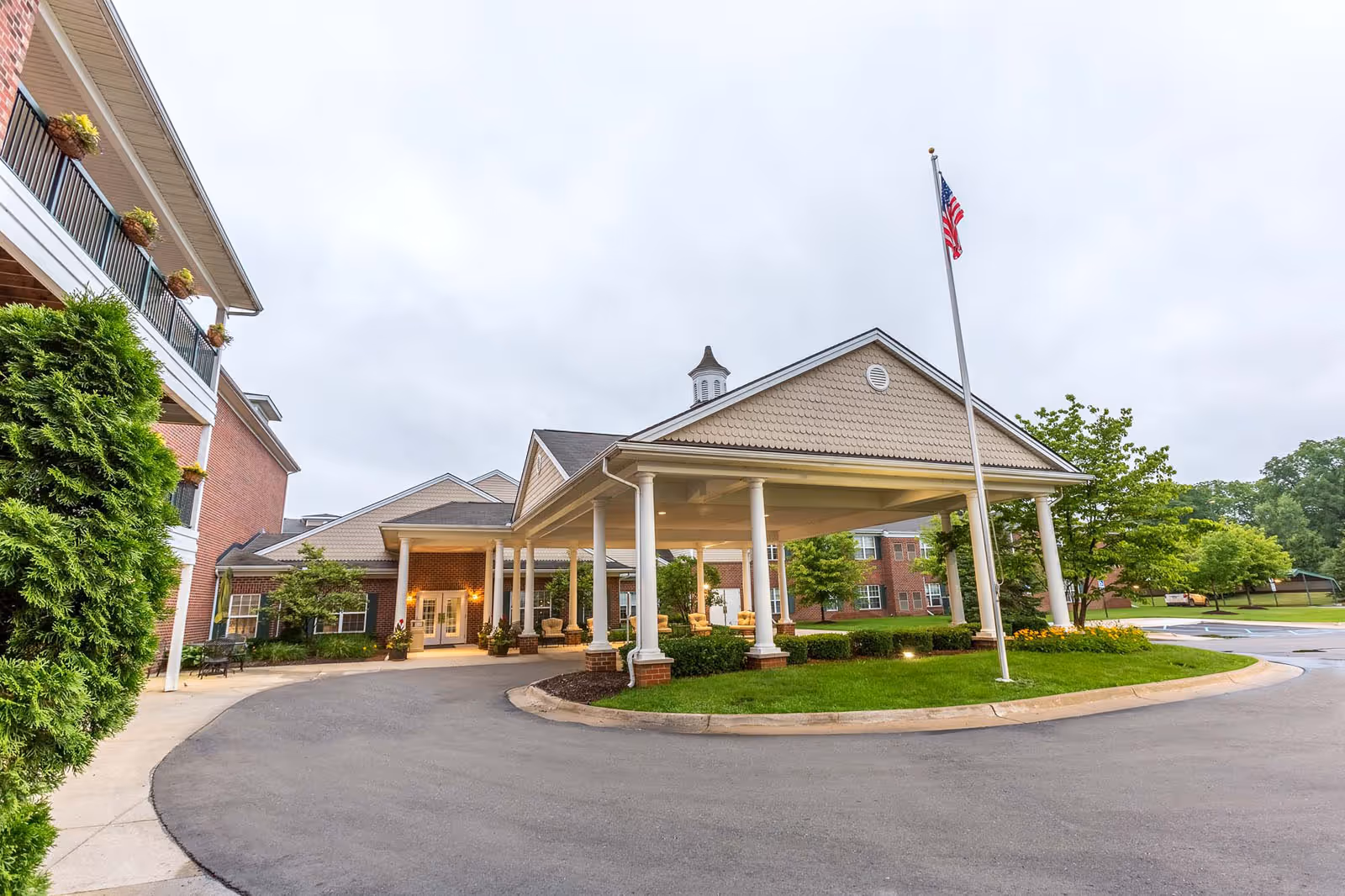 Front entrance of Independence Village of Brighton Valley with a covered porte-cochère, flagpole, and surrounding landscaping.