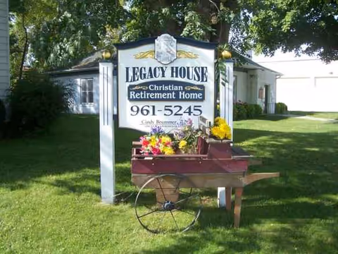 Exterior view of Legacy House sign on a green lawn with flowers.