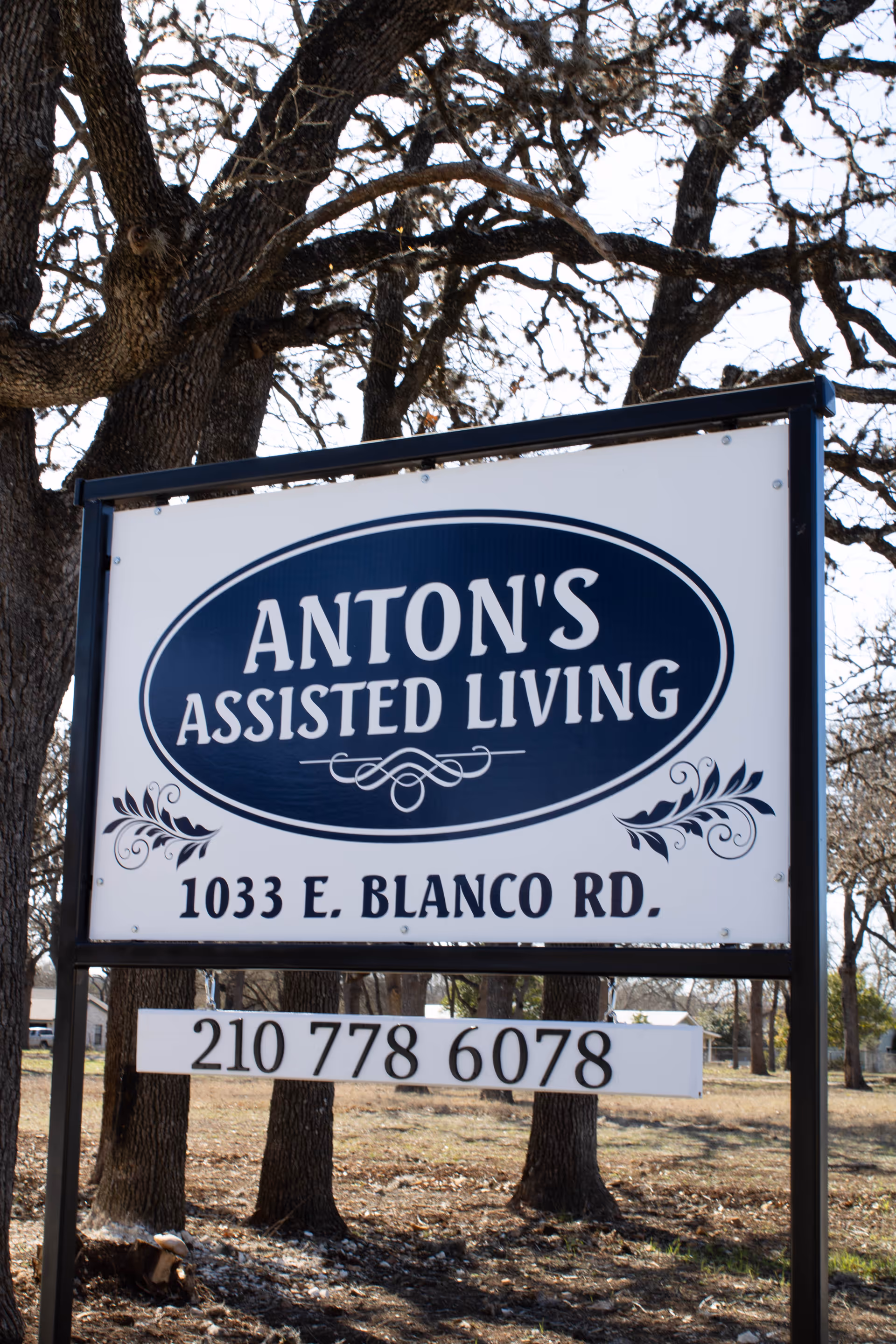 Large outdoor sign for Anton's Assisted Living displaying the address and phone number with trees in the background.