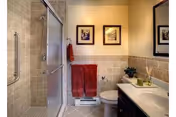 Small bathroom with a glass-enclosed shower, toilet, vanity with sink and mirror, beige tile and red towels.