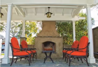 Outdoor covered patio with a stone fireplace, red cushioned chairs, and a small table.