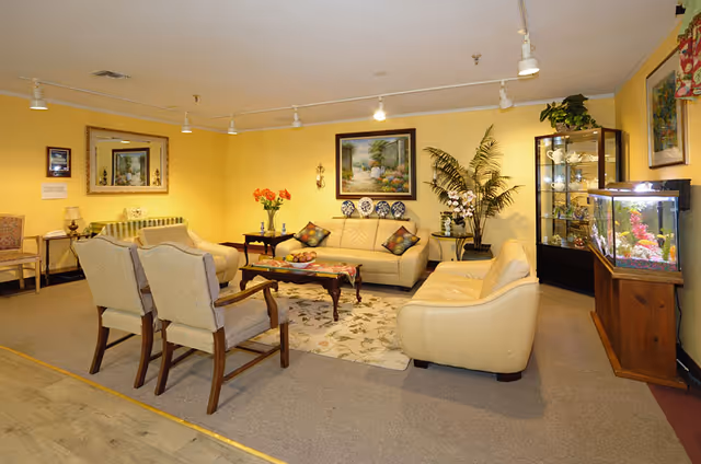 A cozy living room area in a senior living facility featuring comfortable seating, decorative elements, and a fish tank.