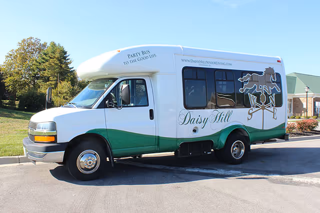 A white and green Daisy Hill Senior Living shuttle van parked outside on a sunny day.