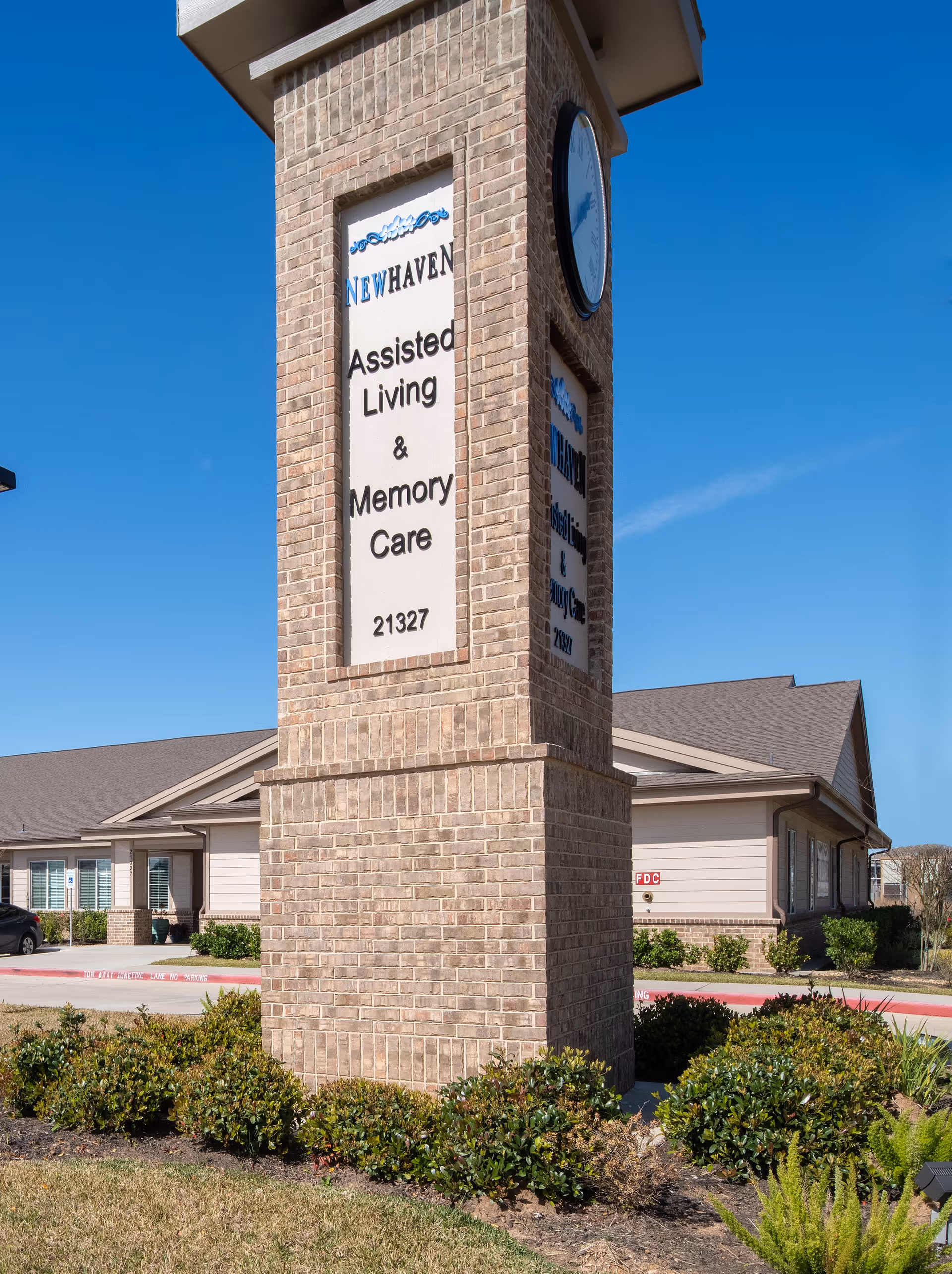Brick entrance tower sign for an assisted living and memory care facility in front of a single-story building under a clear blue sky.