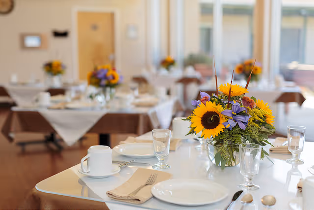 Bright dining room with neatly set tables and sunflower centerpieces.