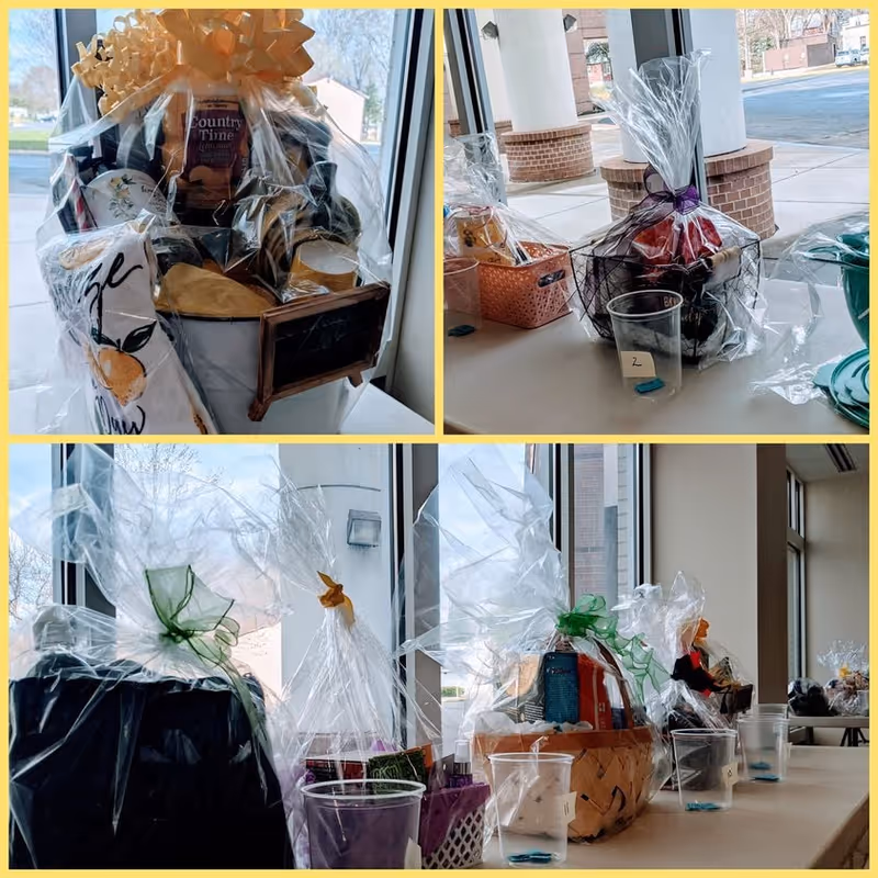 A collage of three images showing various gift baskets wrapped in clear cellophane with decorative bows, displayed on tables near large windows in a bright room. The baskets contain assorted items such as snacks, beverages, and household goods. Clear plastic cups with numbered labels are placed in front of some baskets.