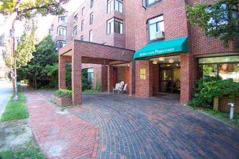 Brick senior living building with a covered entrance and outdoor seating along a brick walkway