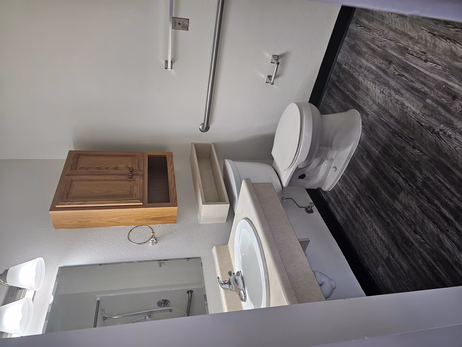 Bathroom with a toilet, sink and vanity, wall-mounted cabinets, grab bars, and dark wood-look flooring.