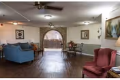A communal lounge with sofas, armchairs, a small dining table, hardwood floors, and an arched doorway.