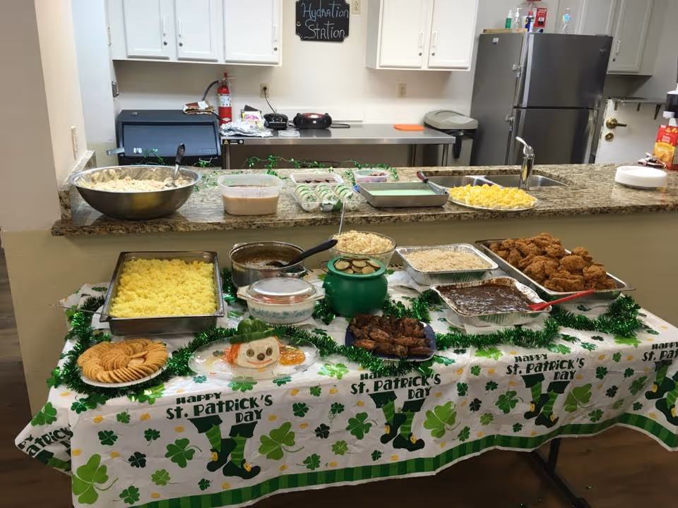 A St. Patrick's Day buffet with trays of food and green decorations set on a table in a facility kitchen/dining area.