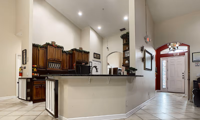 Open interior showing a kitchen island with a dark countertop, wooden cabinets, tiled floor, and a nearby entry door with an EXIT sign.