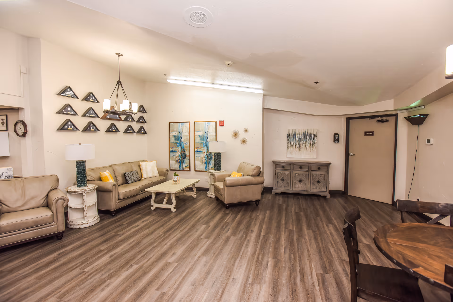 Spacious communal living room with sofas, armchairs, a coffee table, artwork on the walls, and wood-look flooring.