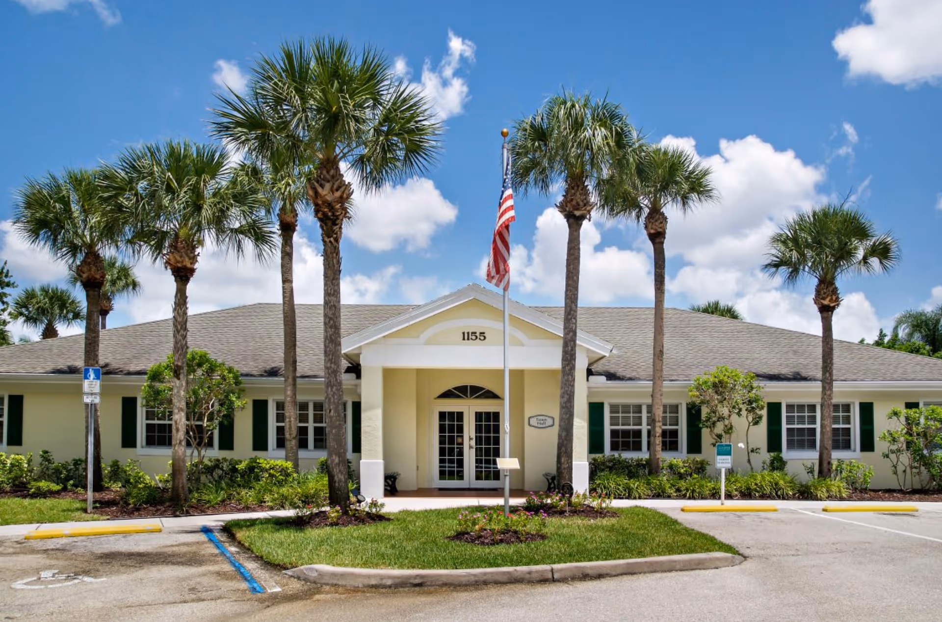 Front view of a single-story yellow building with palm trees, an American flag, and the number 1155 above the entrance.
