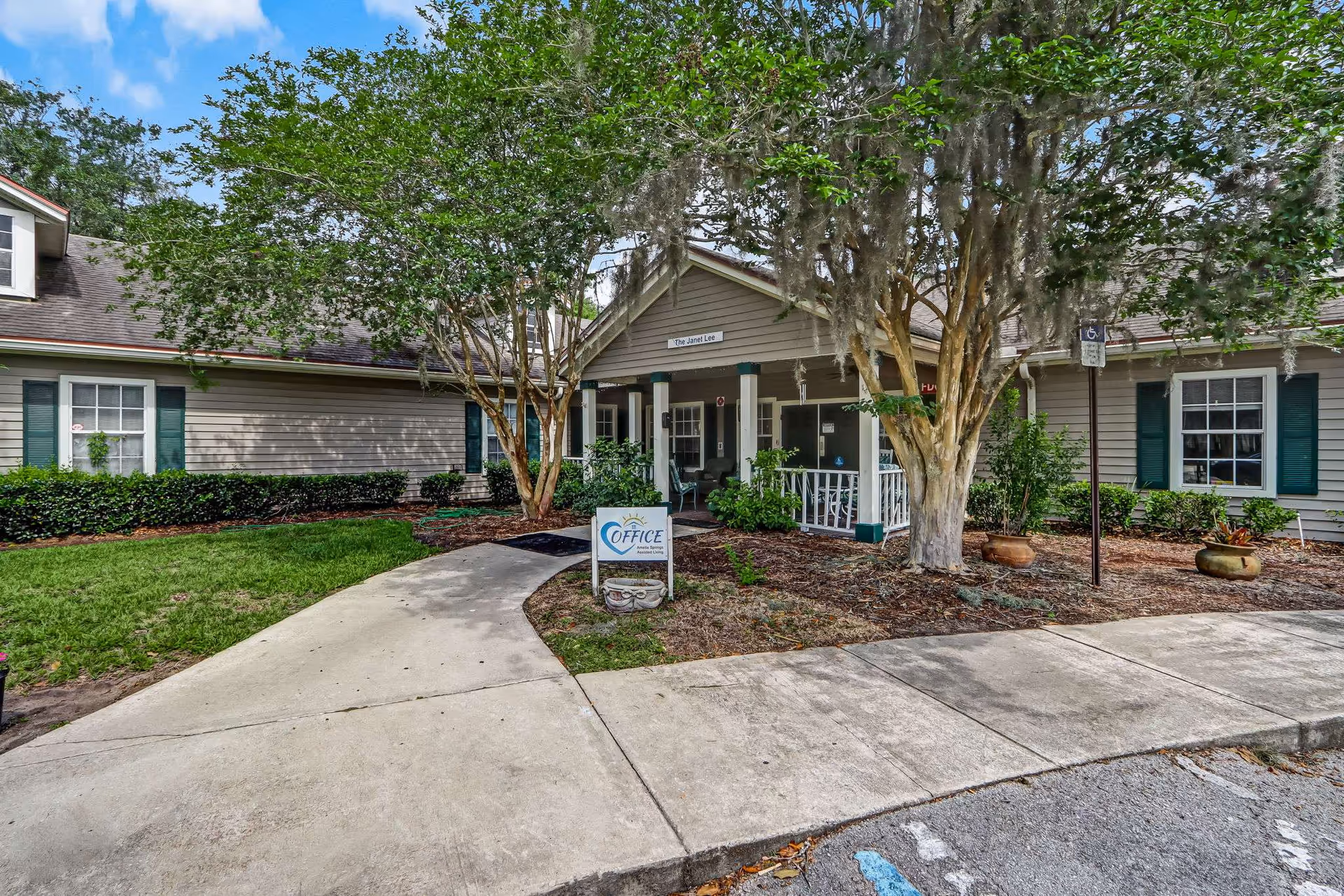Exterior view of Amelia Springs Assisted Living with entrance walkway and trees.