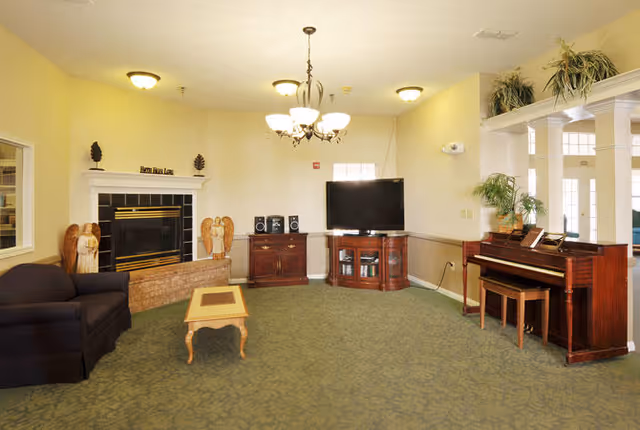 Communal lounge with a fireplace, television, piano, sofa, and coffee table under a chandelier.