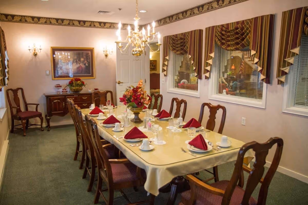 Formal dining room with a long table set with place settings and folded napkins, chandelier overhead and decorative window valances.