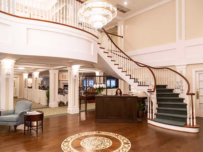 Elegant lobby featuring a sweeping curved staircase, a reception desk, chandelier, and seating area.