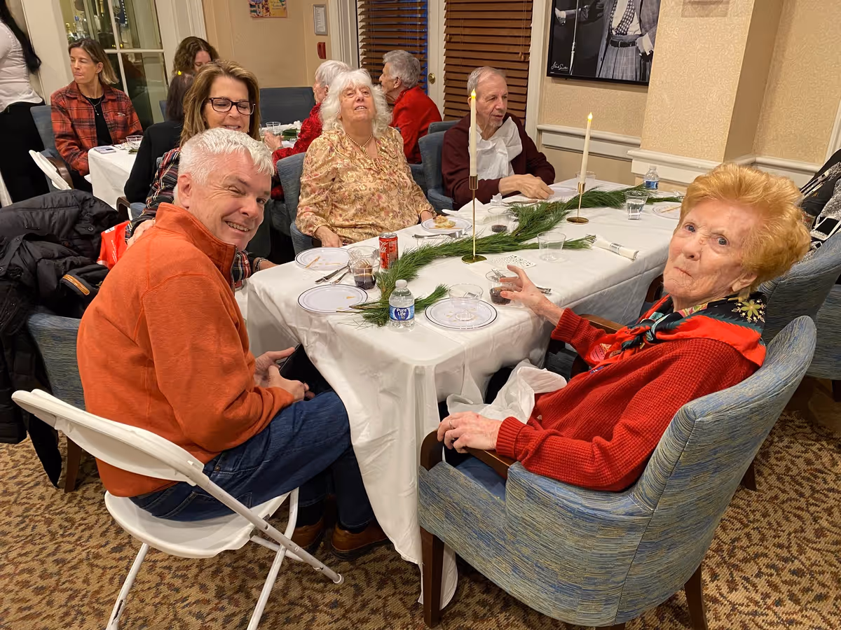 A group of older adults seated around a decorated dining table in a communal dining room.