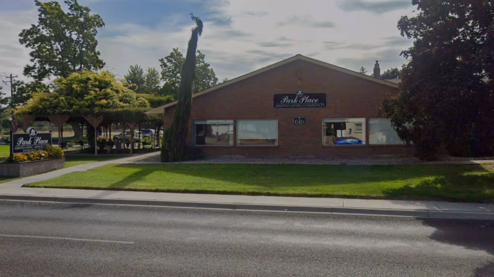 Front exterior of a single-story brick assisted living building labeled 'Park Place' with a lawn, gazebo, and street in front.