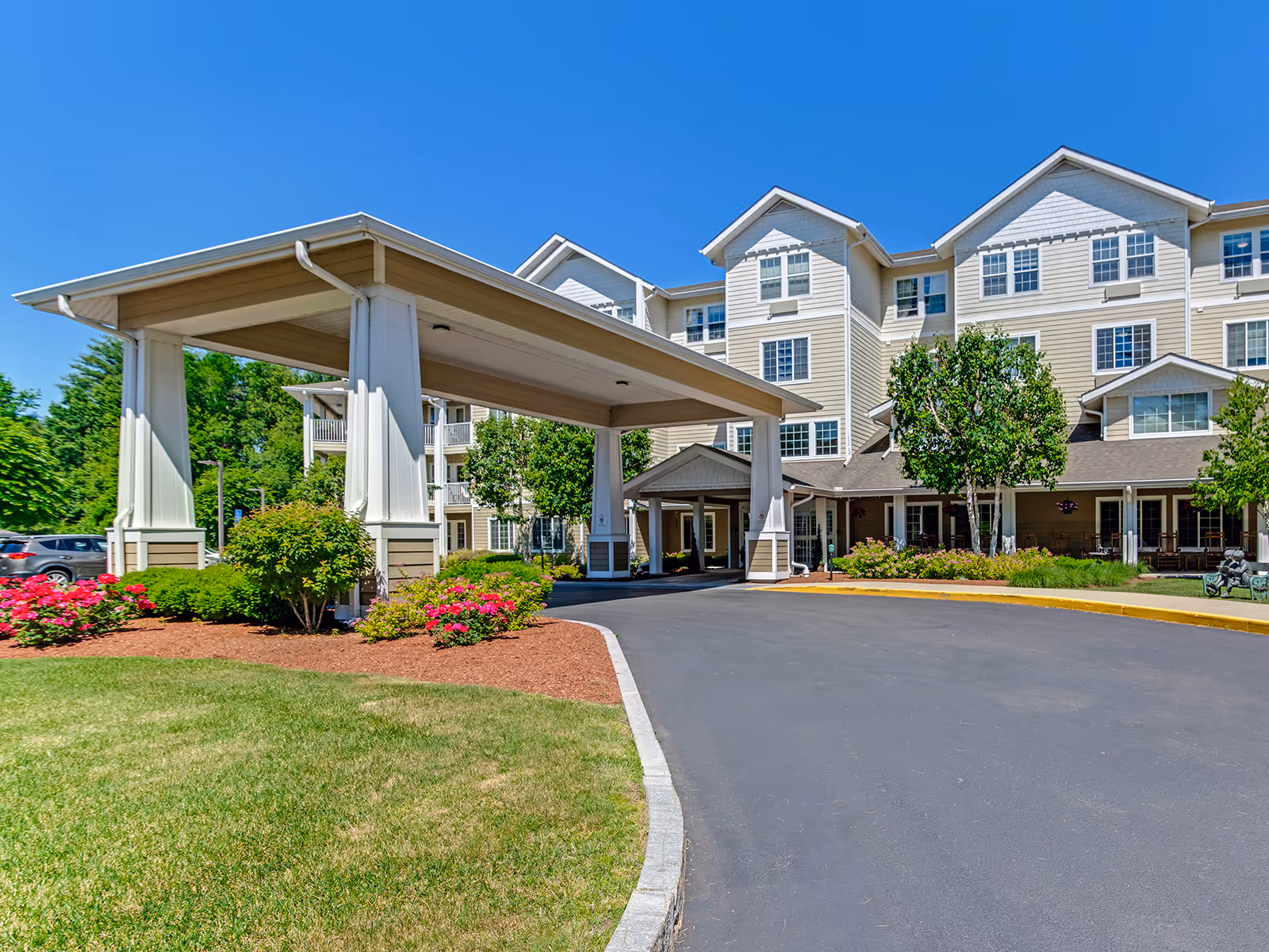 Beige senior living building with a covered entrance and landscaped grounds.