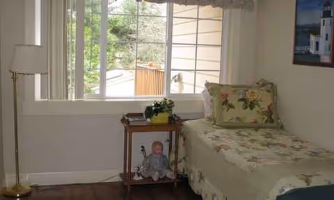 Floral-patterned bedroom in a senior living home with a bed, table, and window.